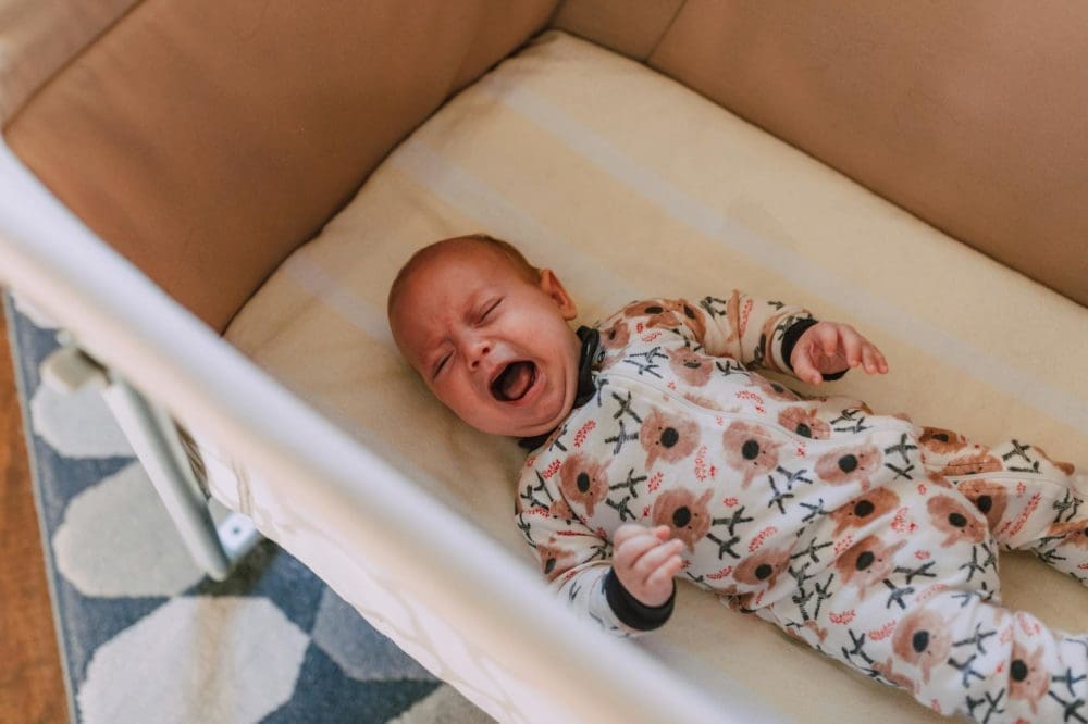 a baby in onesie crying while lying down on crib
